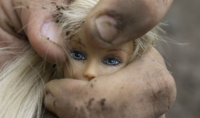 Mano de un hombre adulto con tierra en los dedos sostiene cabeza de muñeca barbie
